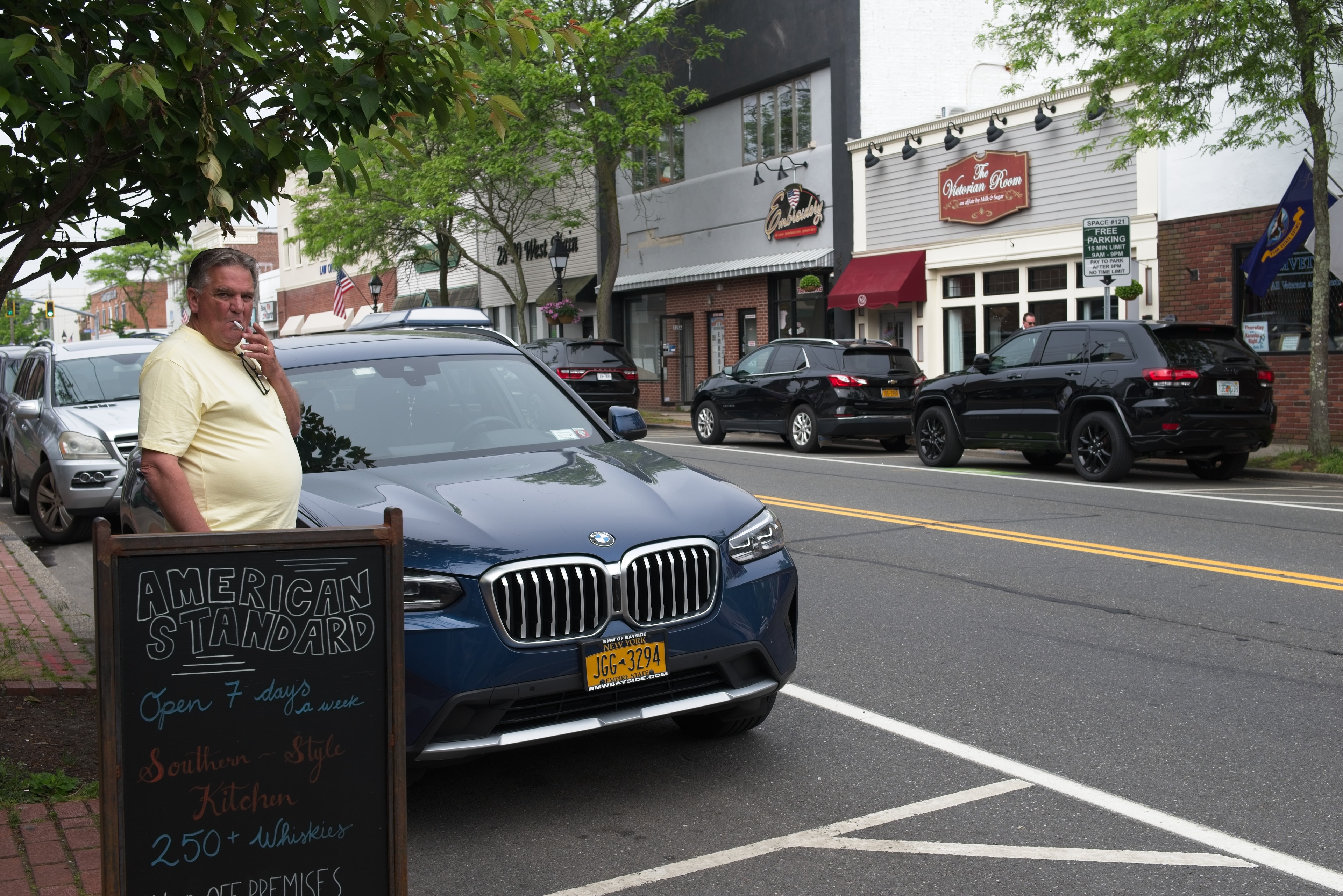 Man smoking beside an American Standard chalkboard sign on a small-town main street
