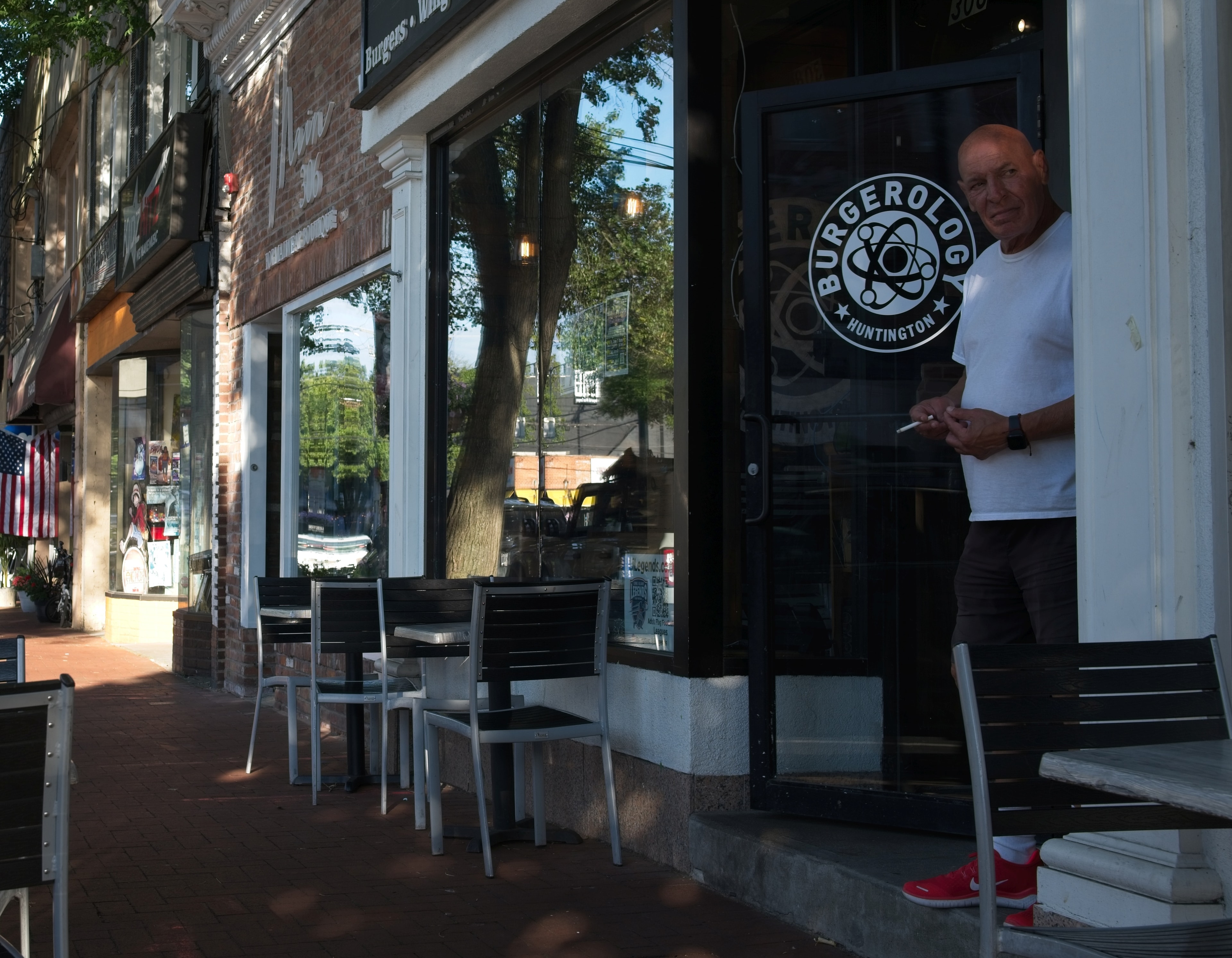 Man leaning in a doorway beside a Burgerolog Huntington sign on a sunny main street