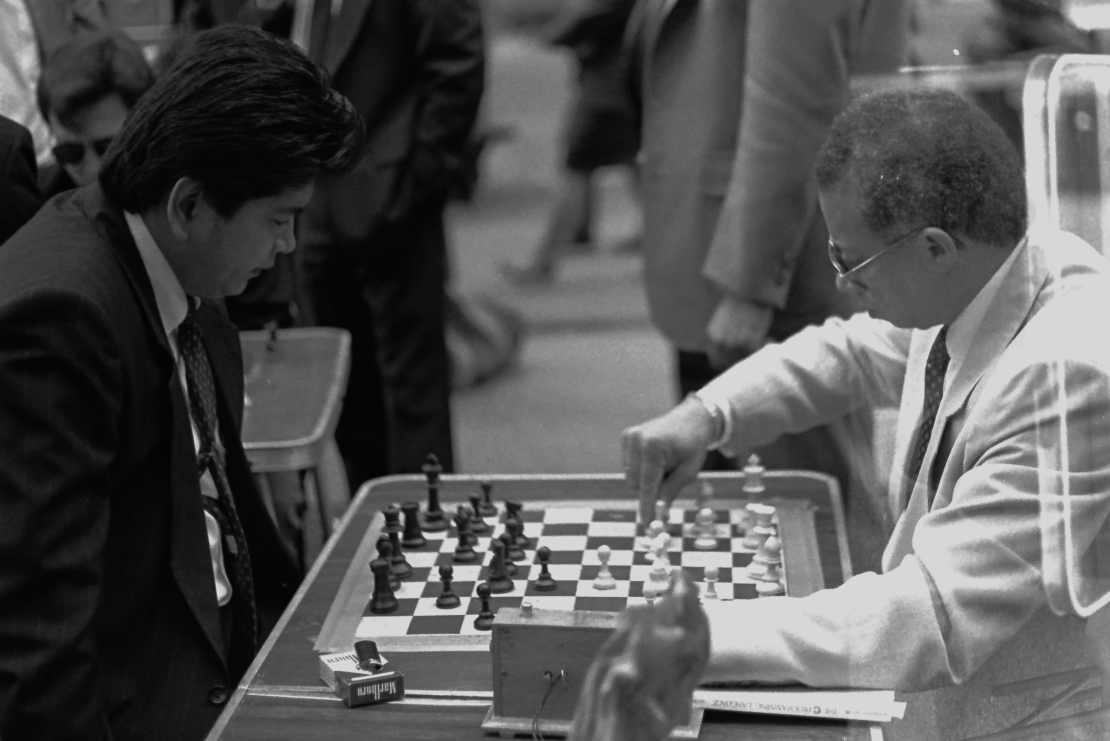 Black and white film photograph of two men in suits intensely focused over a chess board at a public tournament