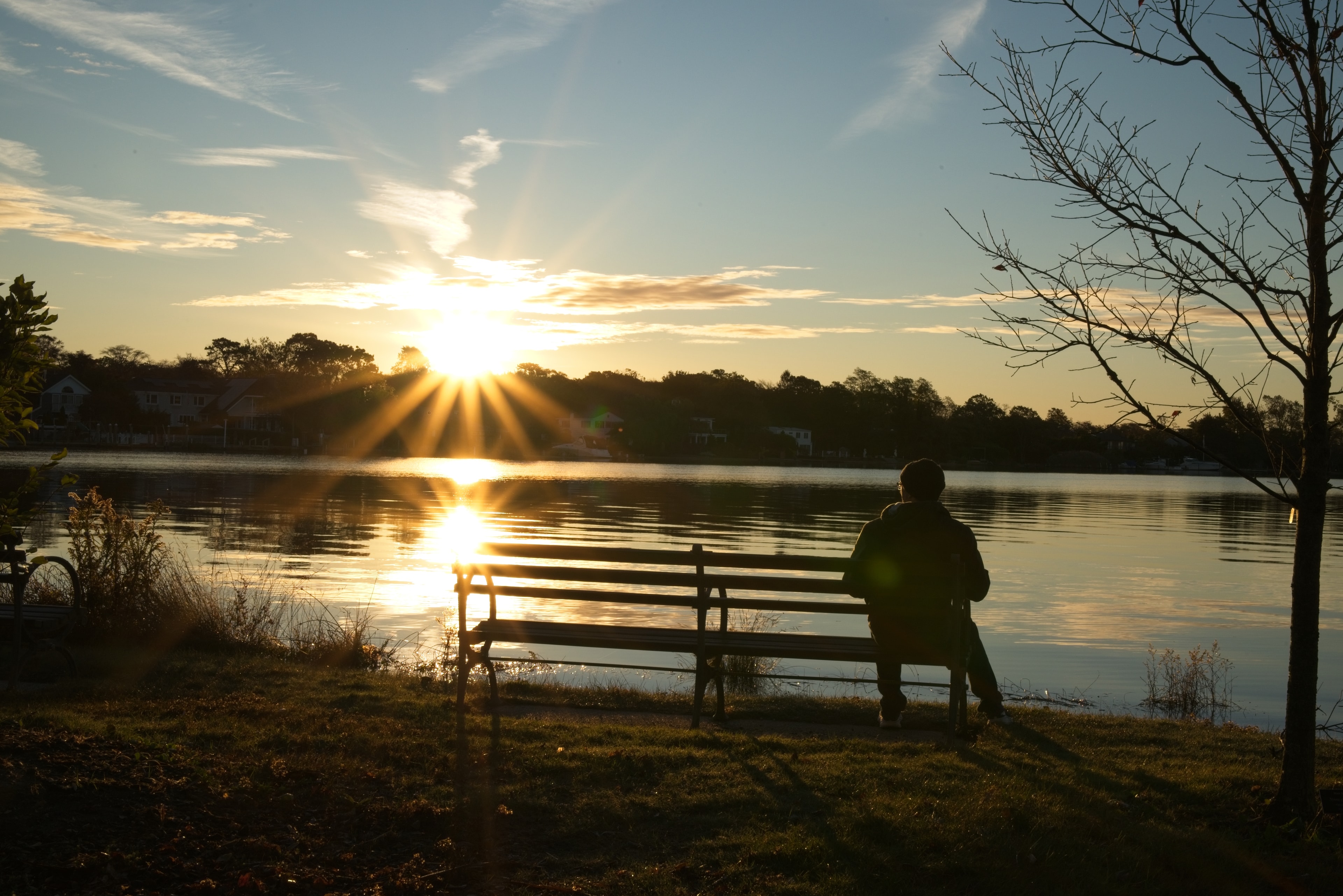 Silhouette of a person on a bench watching a golden sunset over a lake