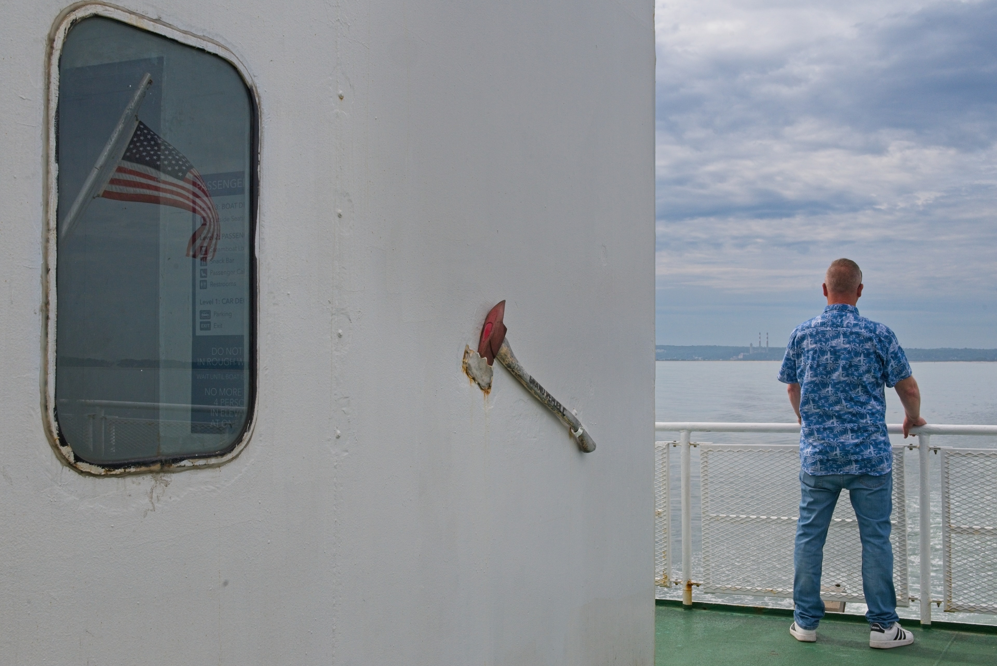 Ferry deck scene with fire axe on wall and man looking out at the water