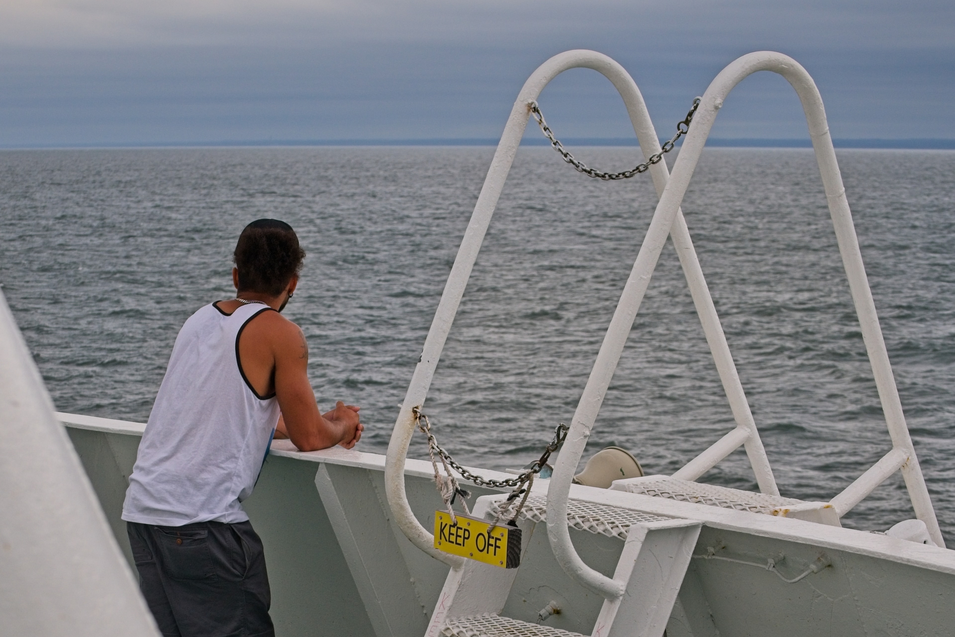 Man in a tank top leaning on a ferry railing gazing out at the open ocean