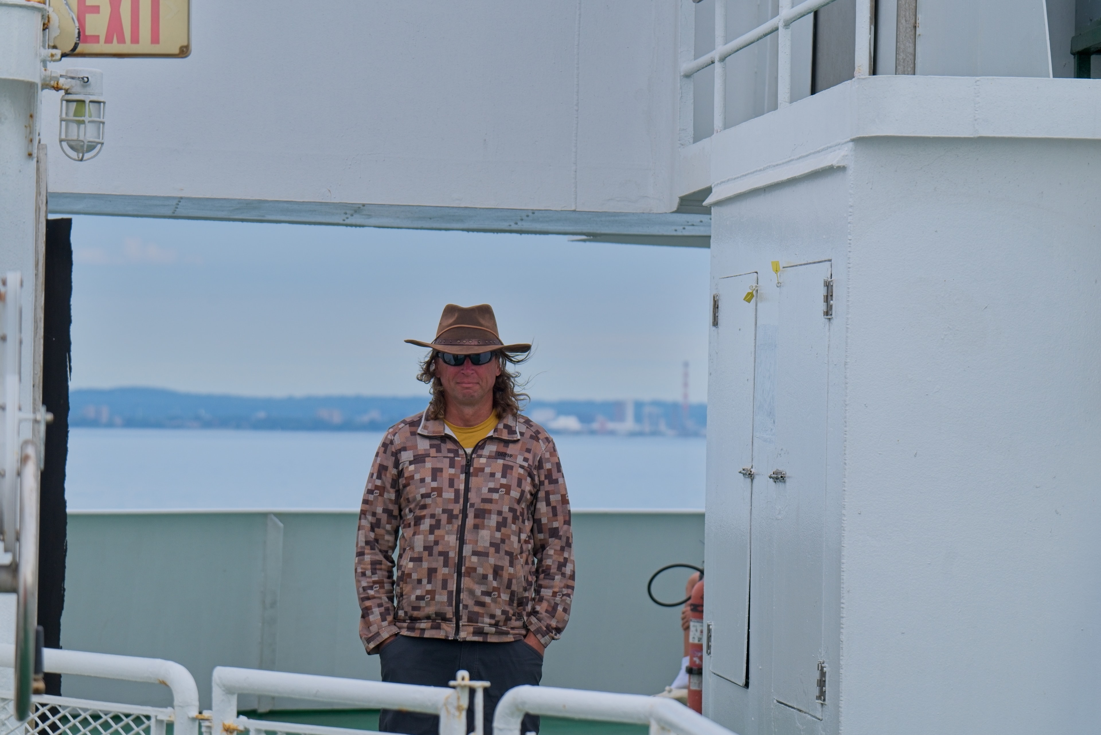Man in a cowboy hat standing on a ferry deck with the water behind him