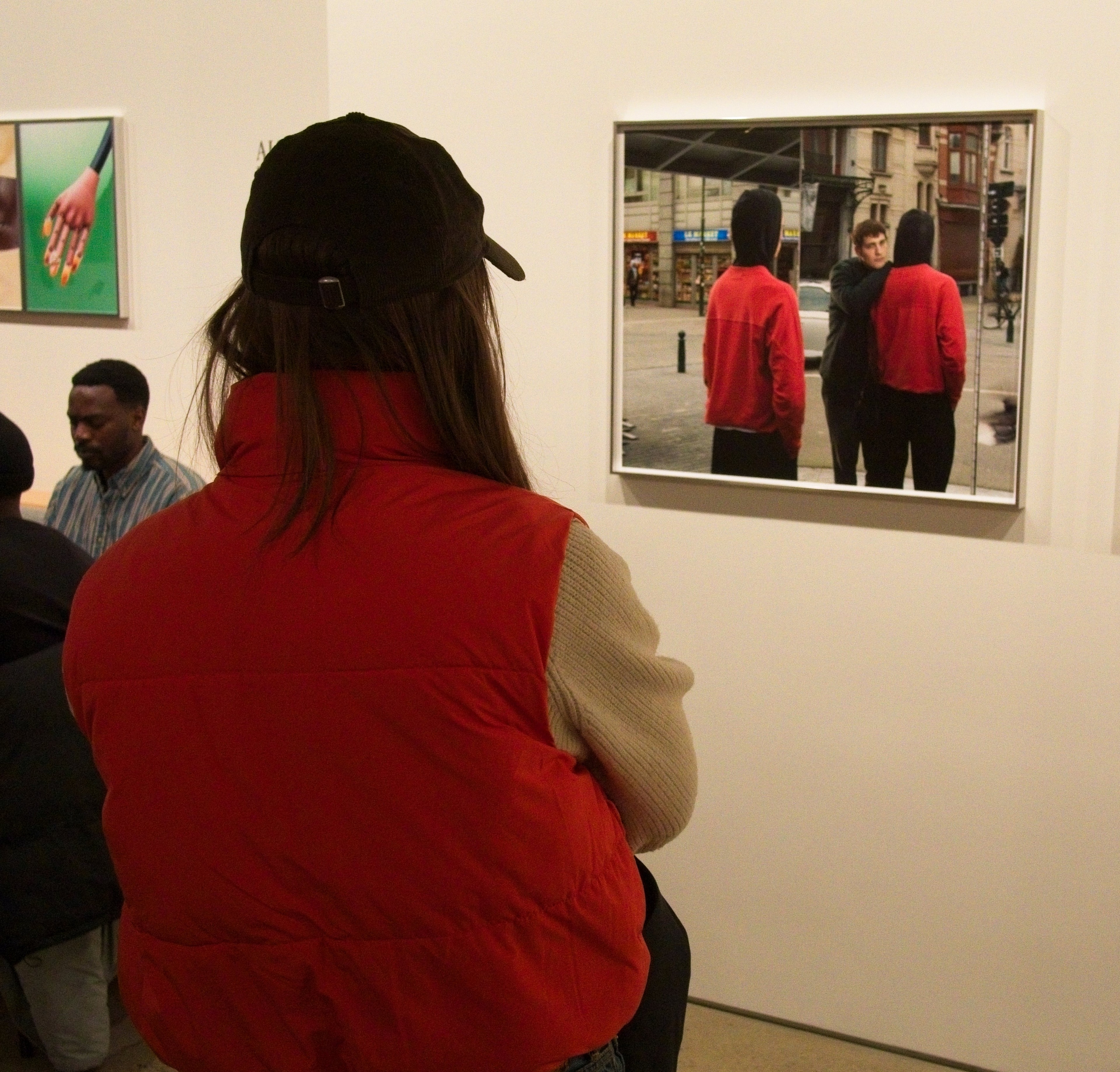 Woman in a red puffer vest studies a large street-photography print at a gallery opening