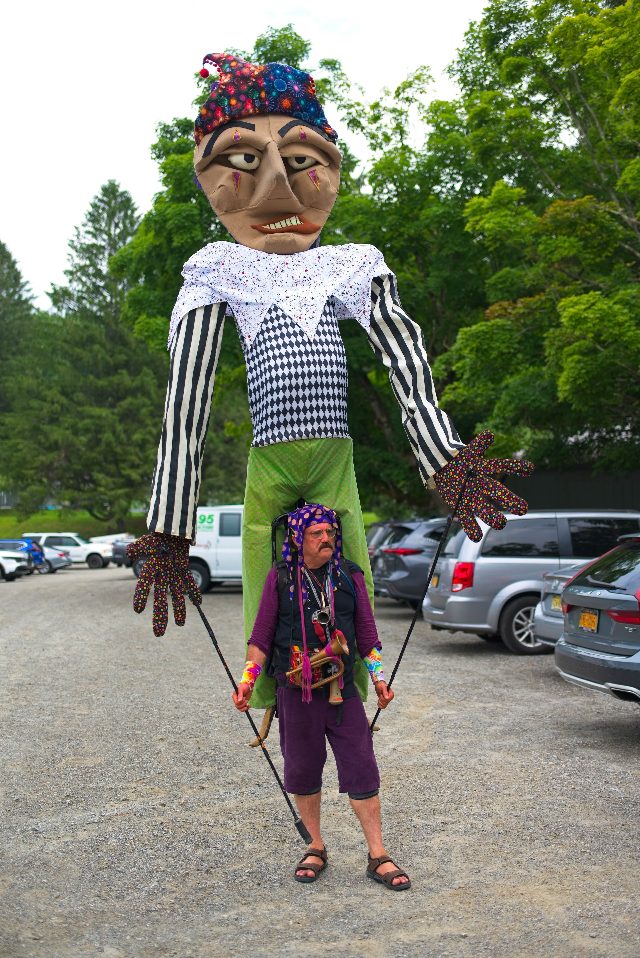 Street performer operating a towering jester puppet in a parking lot