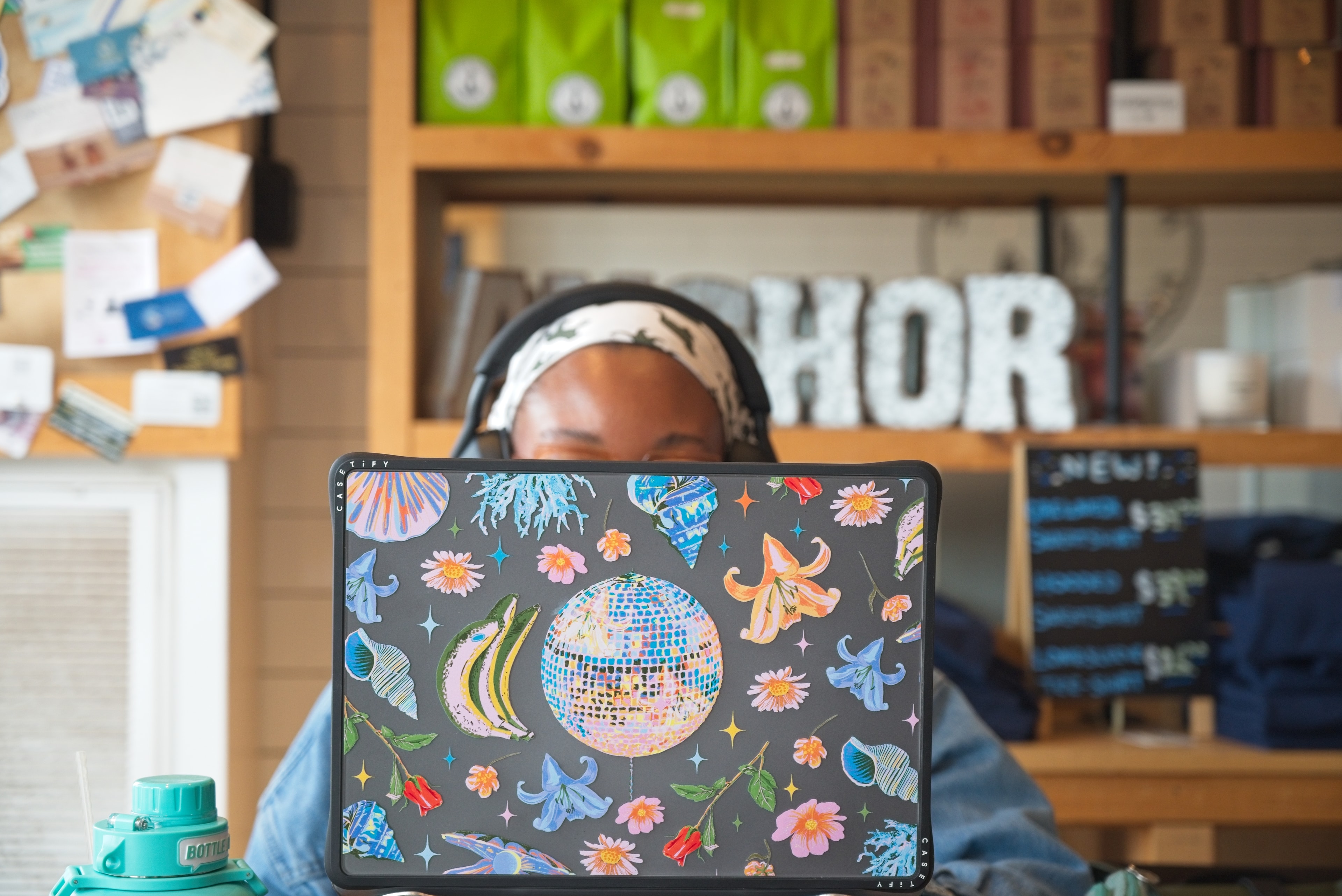 Person behind a colorfully illustrated laptop case in a coffee shop