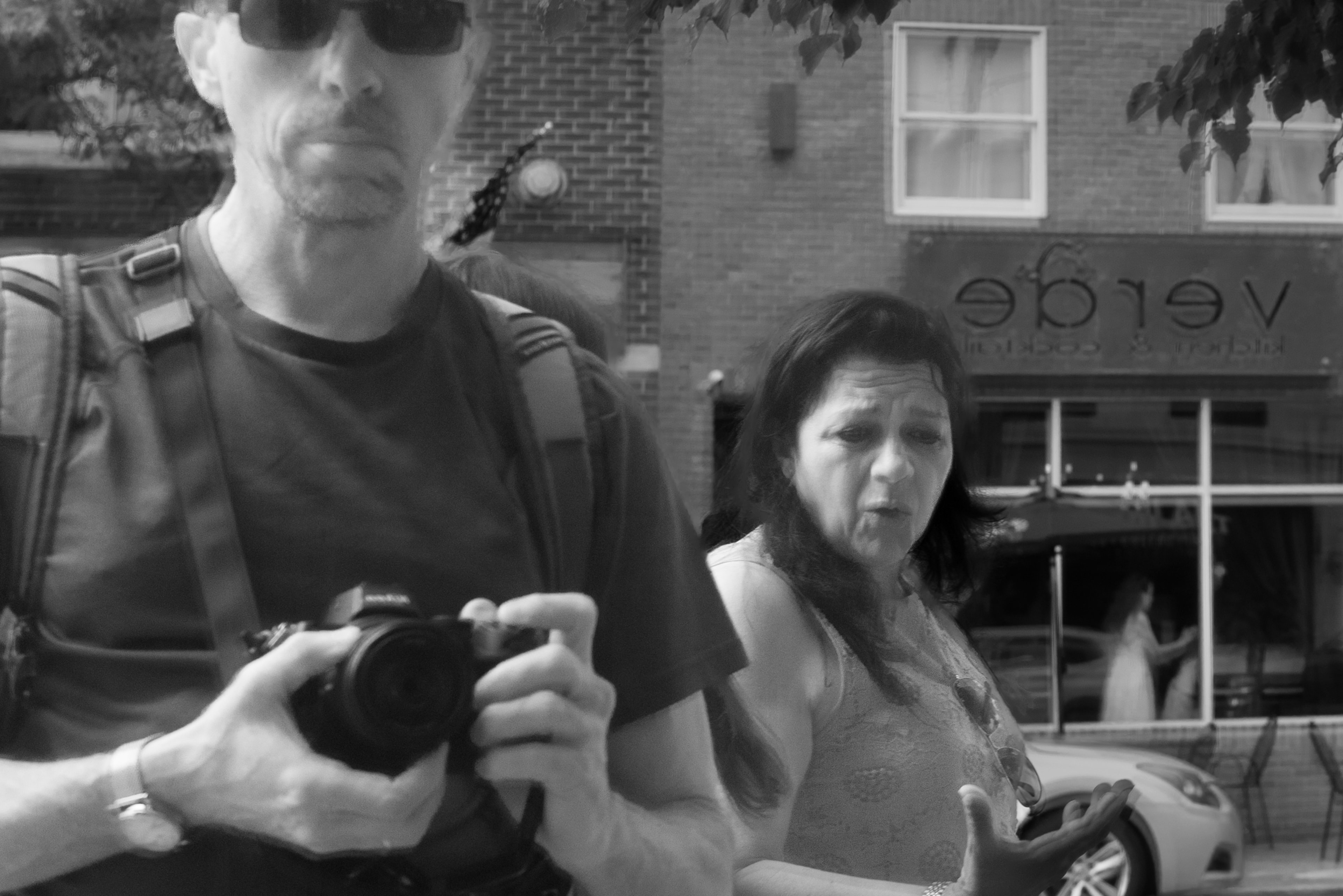 Black and white candid of a photographer and a woman reacting on a city street