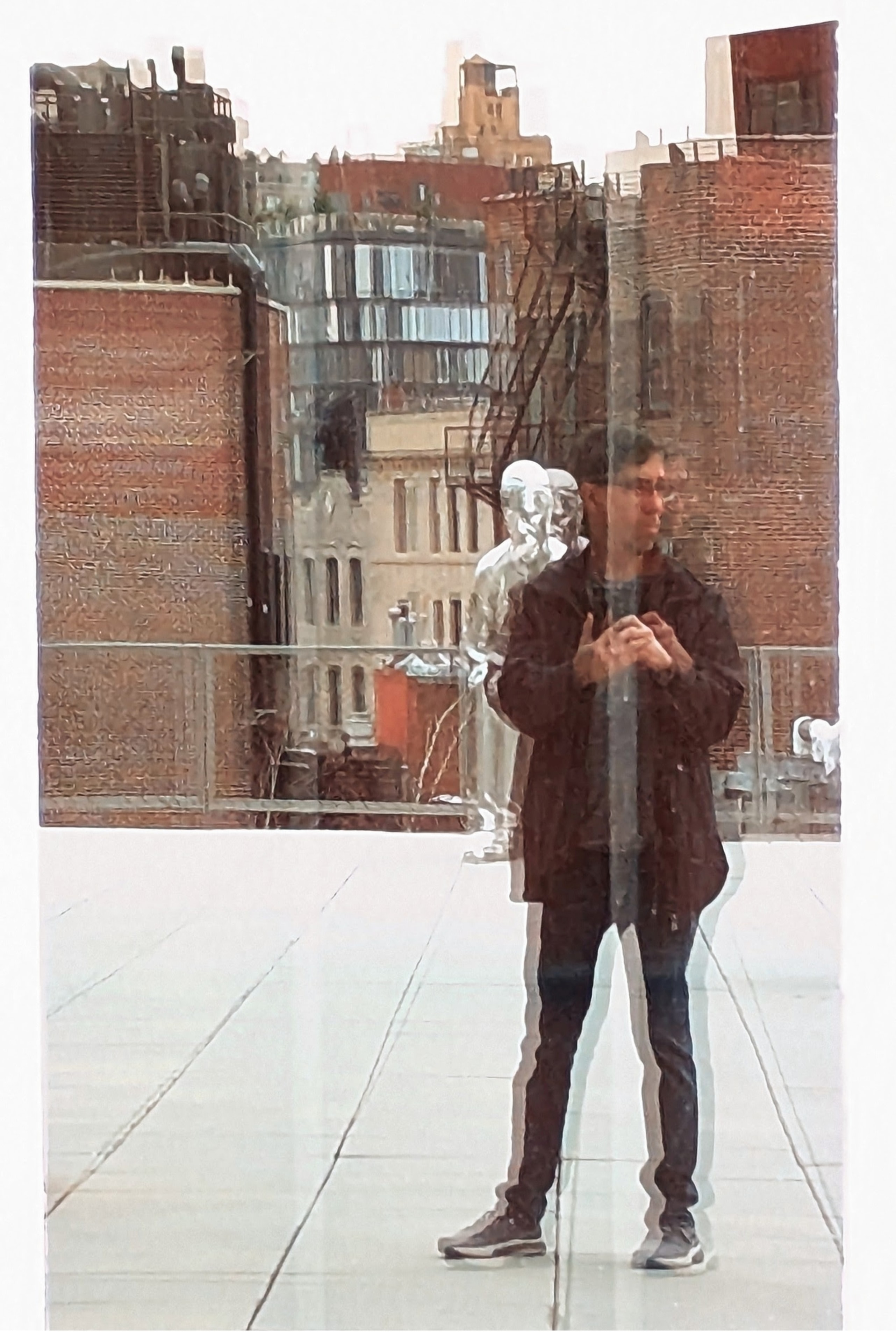 Man reflected and refracted through a glass panel on a rooftop terrace with NYC brick buildings behind him