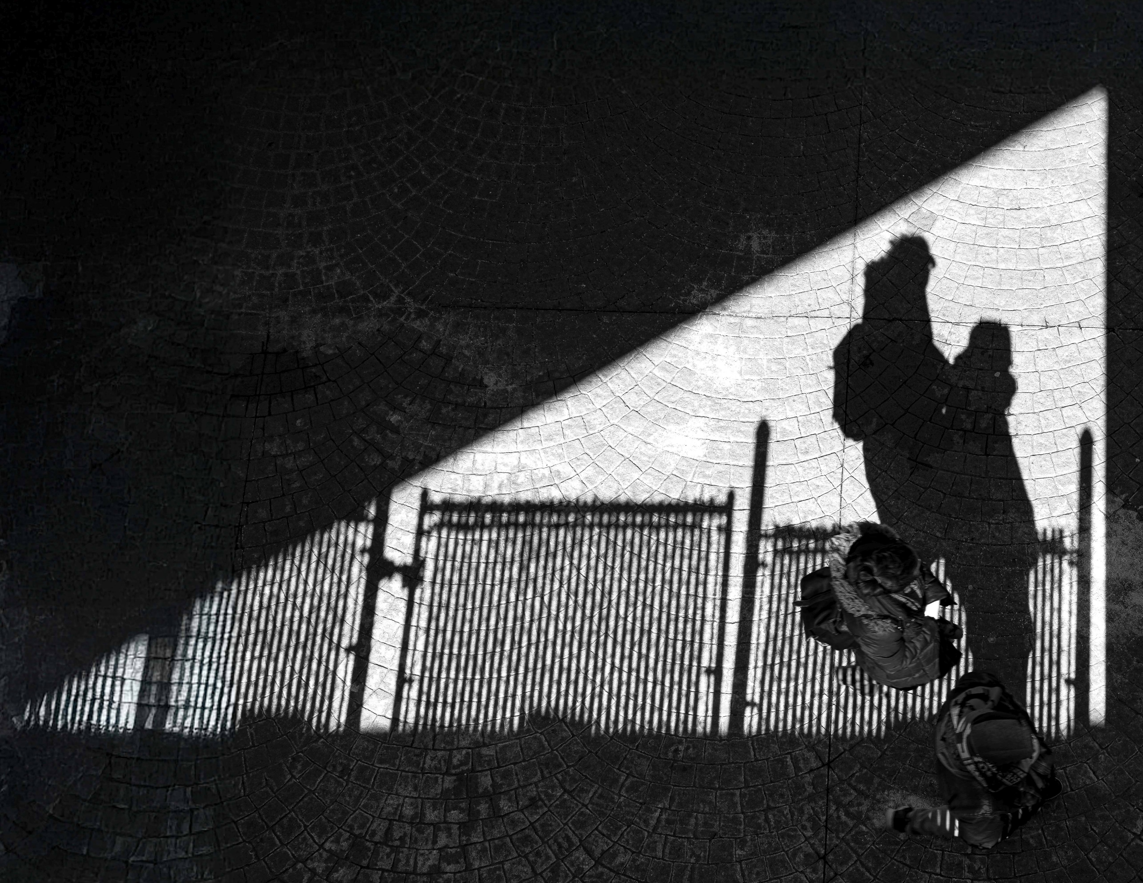 Dramatic black and white shadows of two figures cast across cobblestone pavement