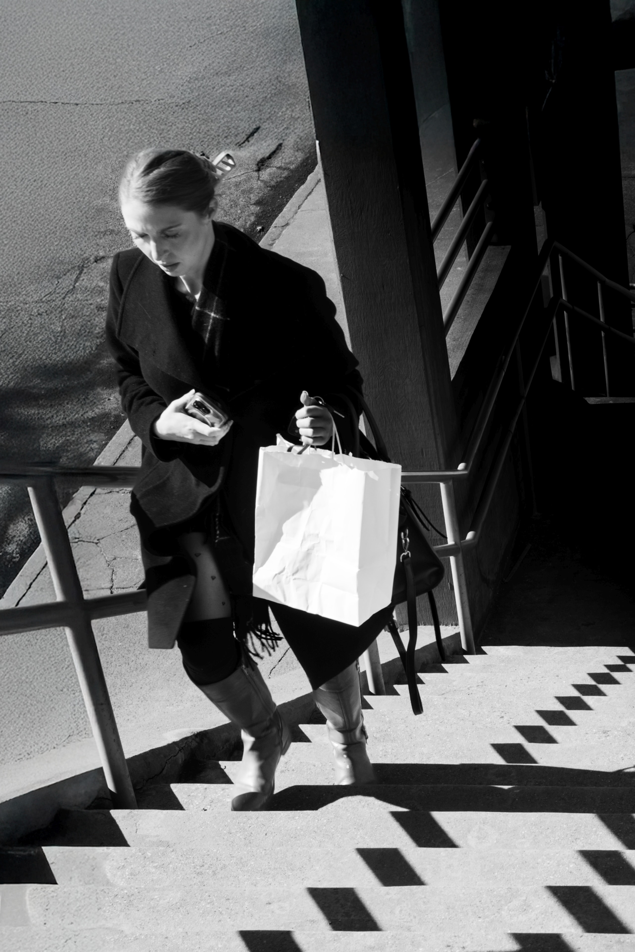 Black and white overhead shot of a woman descending stairs with a shopping bag